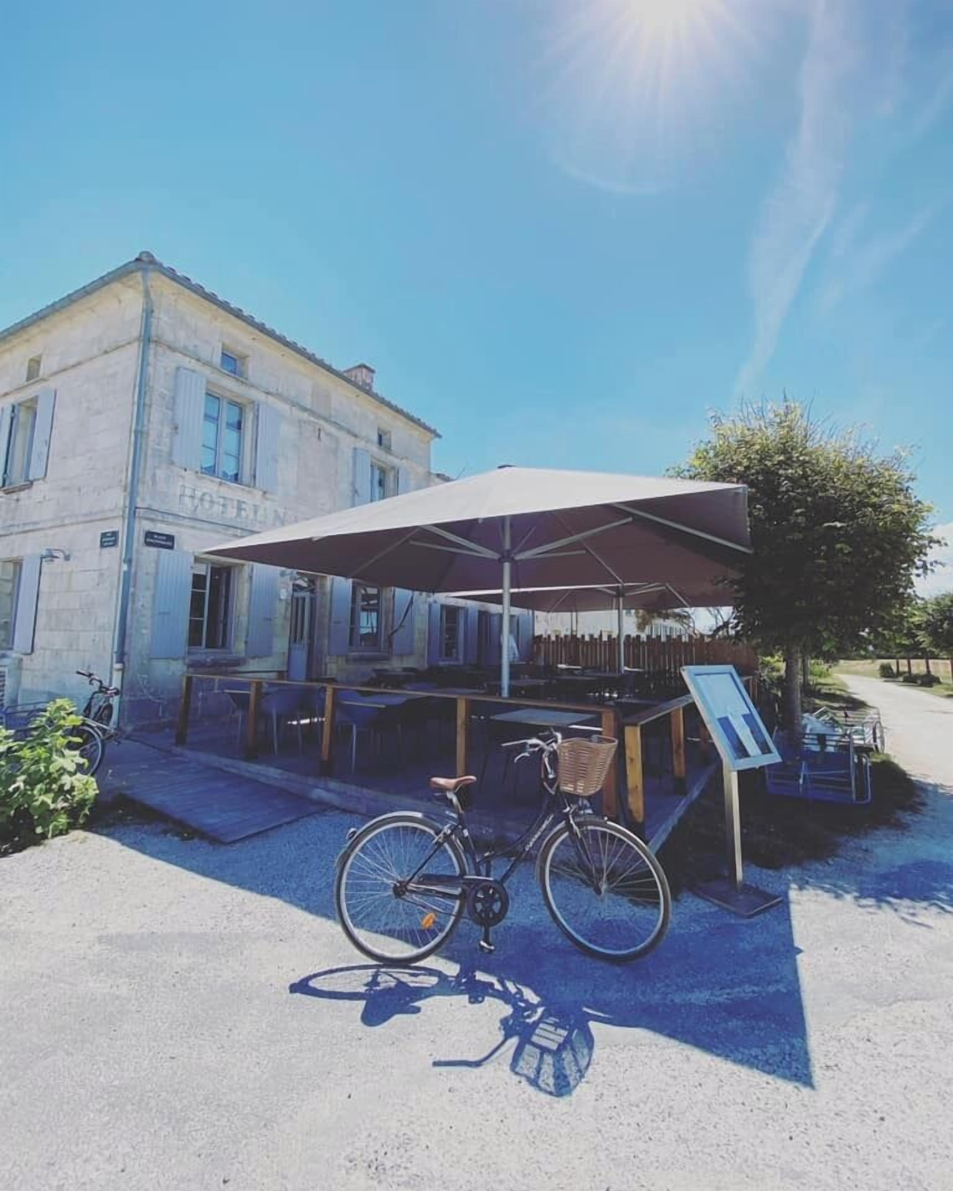 Una bicicleta estacionada bajo una marquesina en un puesto a la vera de la carretera con un letrero, frente a un edificio que dice "HOTEL".
