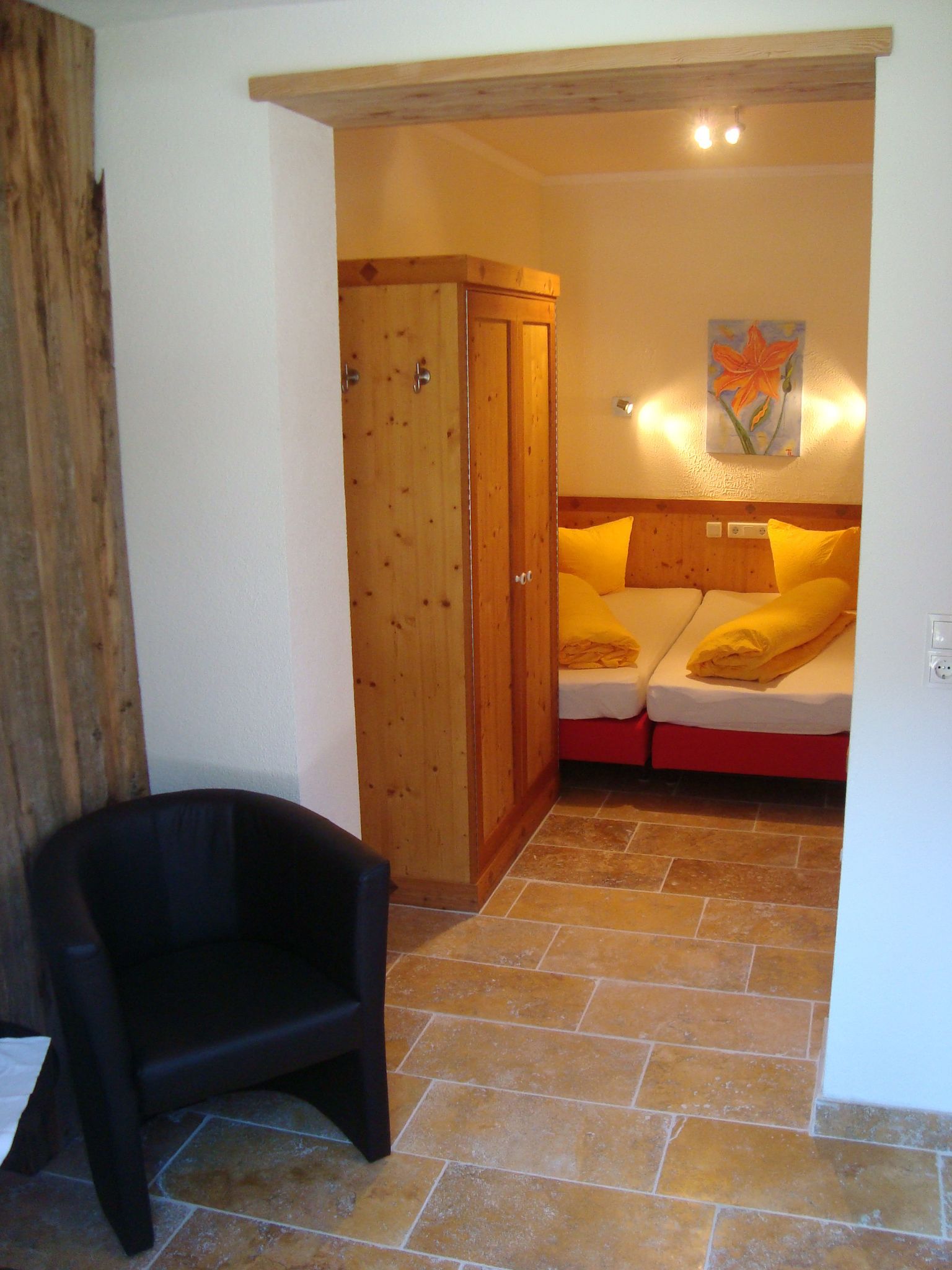 A bedroom with a wooden wardrobe, a bed with yellow bedding, and a painting on the wall.