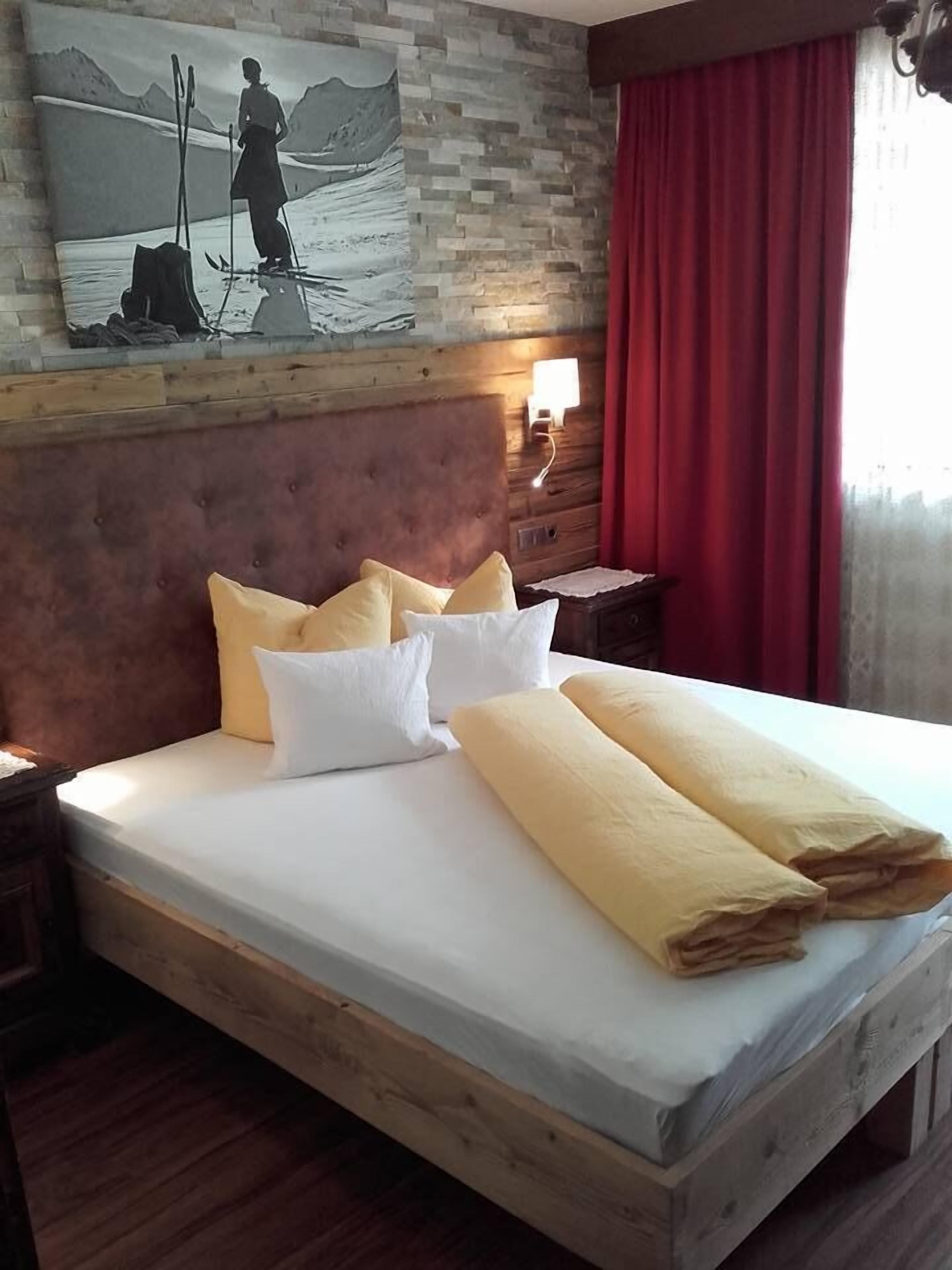 A bed with white and yellow linens, a wooden headboard, and a painting of a skier on the wall.
