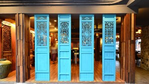 Una porta in legno tradizionale con elaborate incisioni, che dà accesso a una stanza con pavimento in legno e parete in pietra.