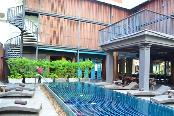 Un espace piscine aménagé sur le toit, avec des chaises longues, un escalier en colimaçon et une façade en bois.