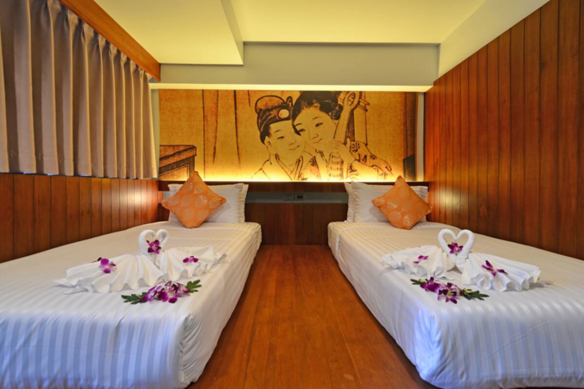 A hotel room with two beds, wooden paneling, and a mural on the wall.