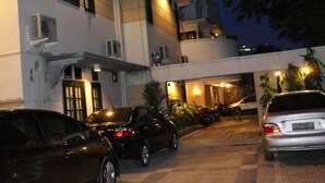 Ein mehrstöckiges Gebäude mit Parkplatz davor. Mehrere Autos sind geparkt, und das Gebäude verfügt über viele Fenster und Klimaanlagen.