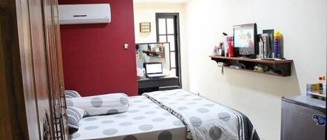 A bedroom with a bed, a desk, a chair, a TV, and a refrigerator.