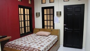Ein Schlafzimmer mit einem Bett, einem Nachttisch, einer Holzkommode, einer roten Wand und einer schwarzen Tür.