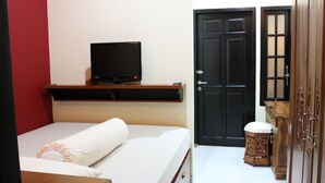 Ein Schlafzimmer mit einem Bett, einem Fernseher auf einem Regal, einer Tür und einem kleinen Hocker.