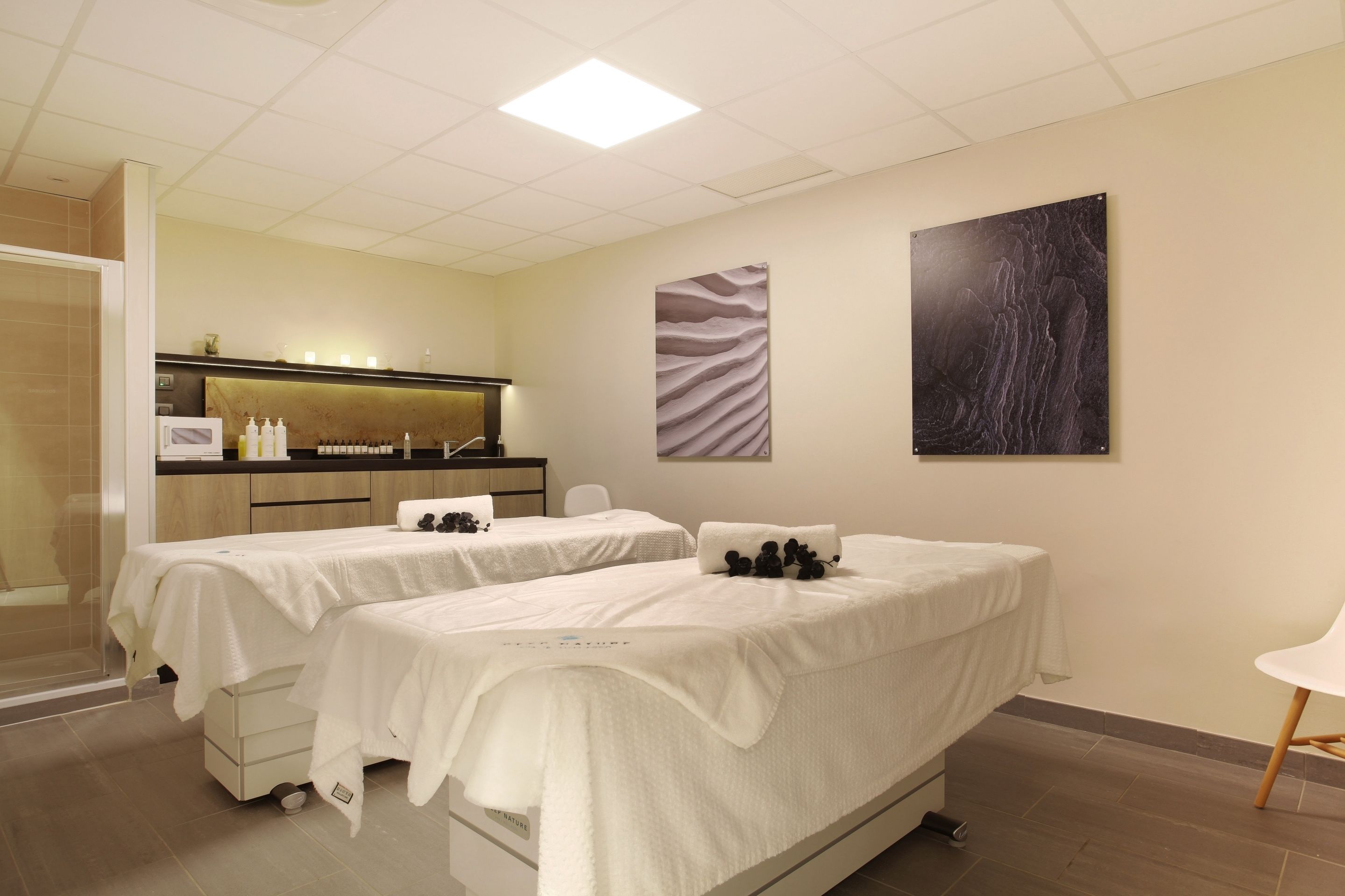 Une salle de spa comprenant deux tables de massage, un comptoir d’accueil et une œuvre d’art fixée au mur.