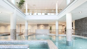 A multi-level indoor swimming pool with clear water, tiled steps, and a stone wall.