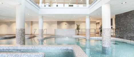 A multi-level indoor swimming pool with clear water, tiled steps, and a stone wall.
