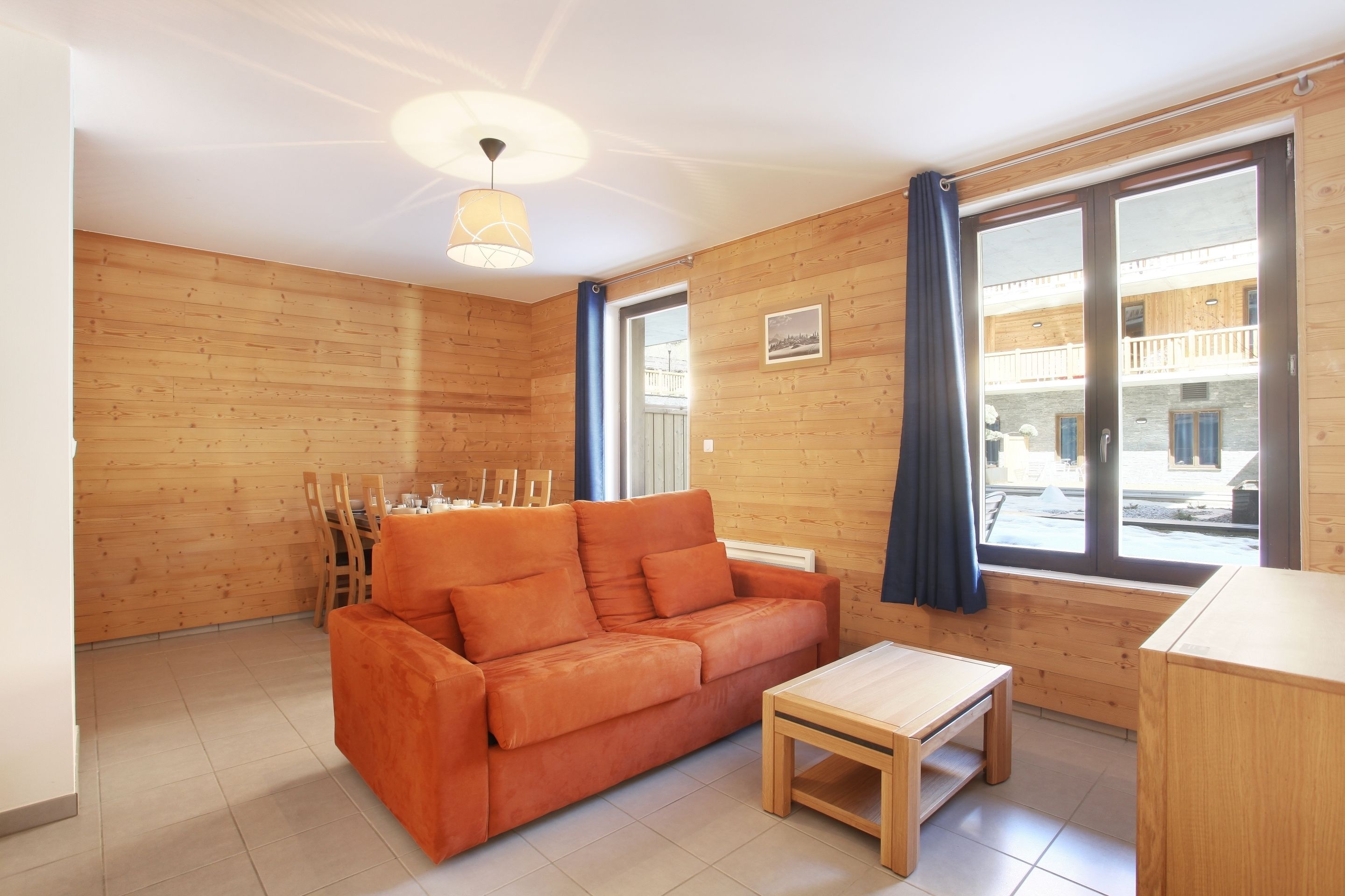 Un salon chaleureux avec un mur en bois, un canapé, une petite table et de grandes fenêtres avec des rideaux.