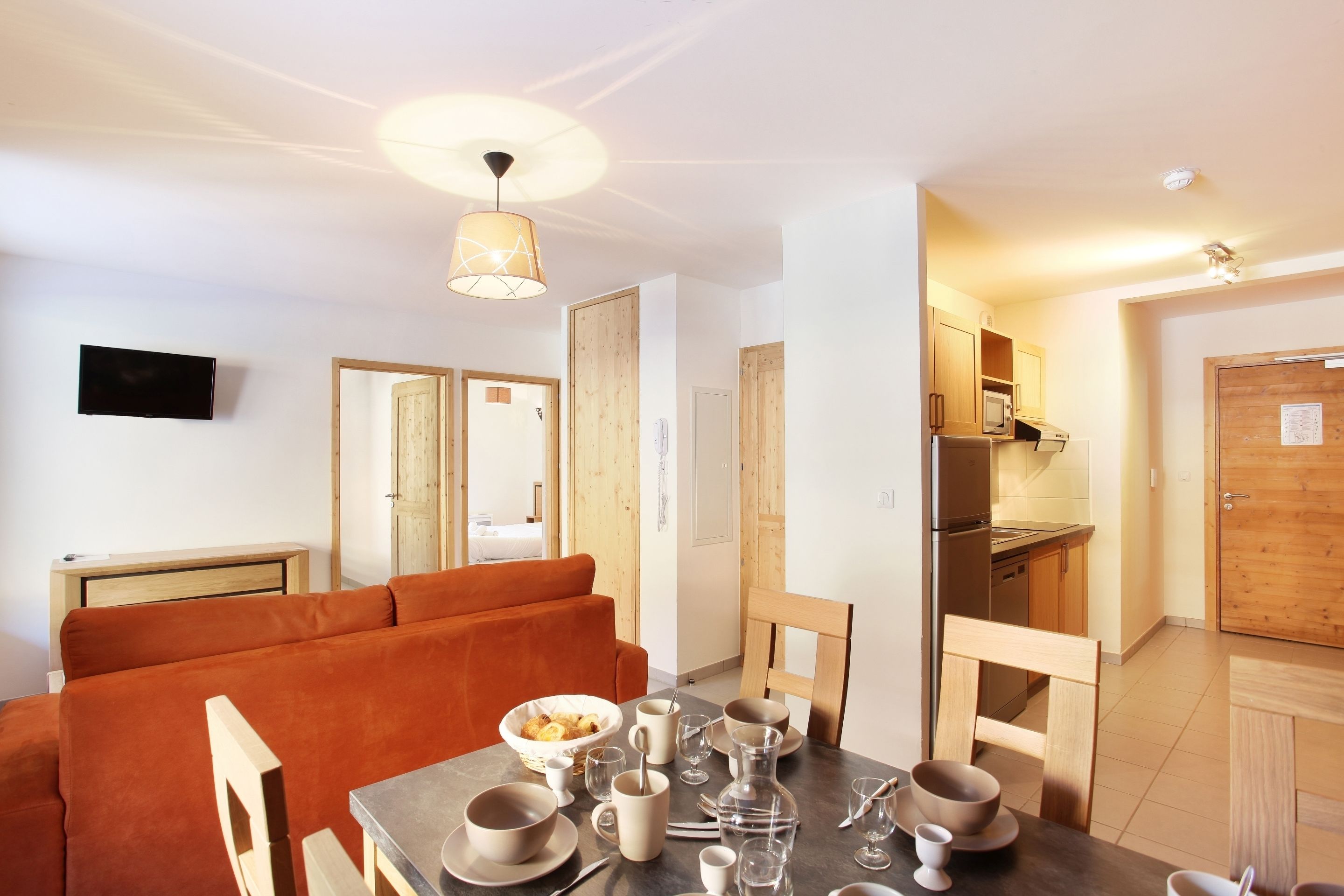 Una cocina moderna con armarios de madera, horno empotrado y comedor con mesa lista para cuatro comensales.