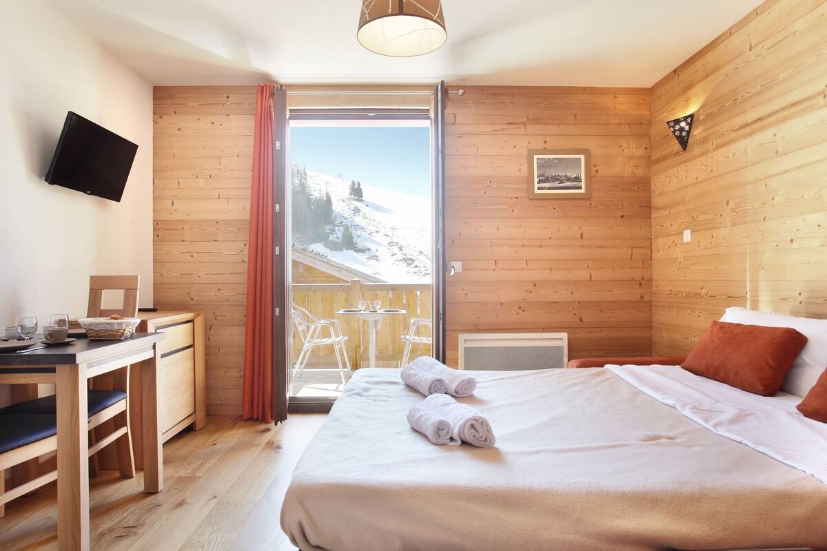Een gezellige kamer met een bed, een bureau en een televisie. Er is een raam met uitzicht op een besneeerd landschap.