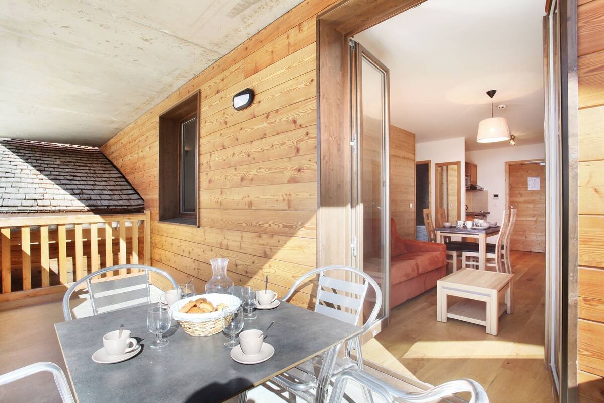 Een houten chalet met een eethoek, voorzien van een tafel gedekt met witte borden, glazen en een mand met brood.