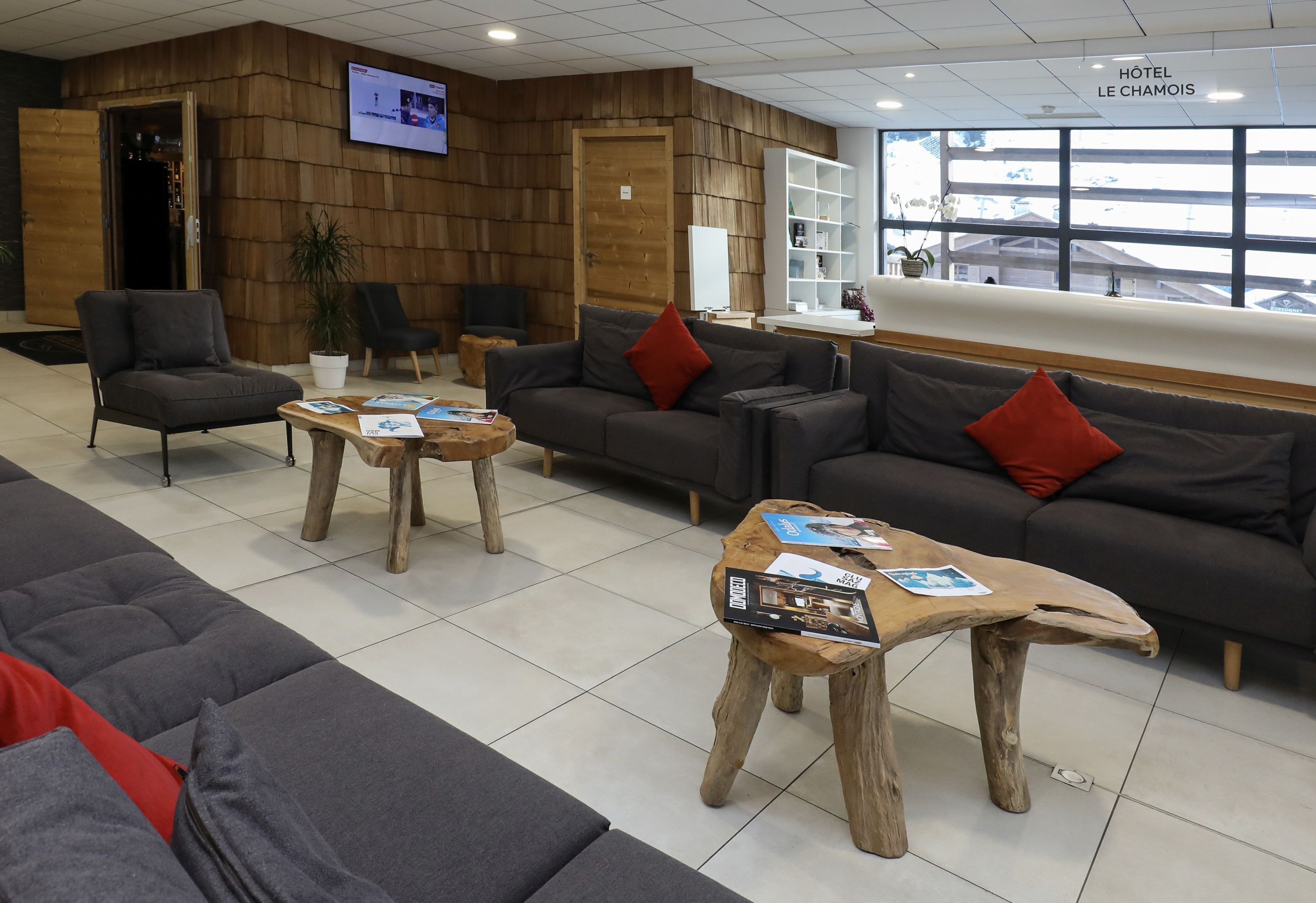 A hotel lobby with sofas, chairs, a wooden coffee table, and a TV screen.