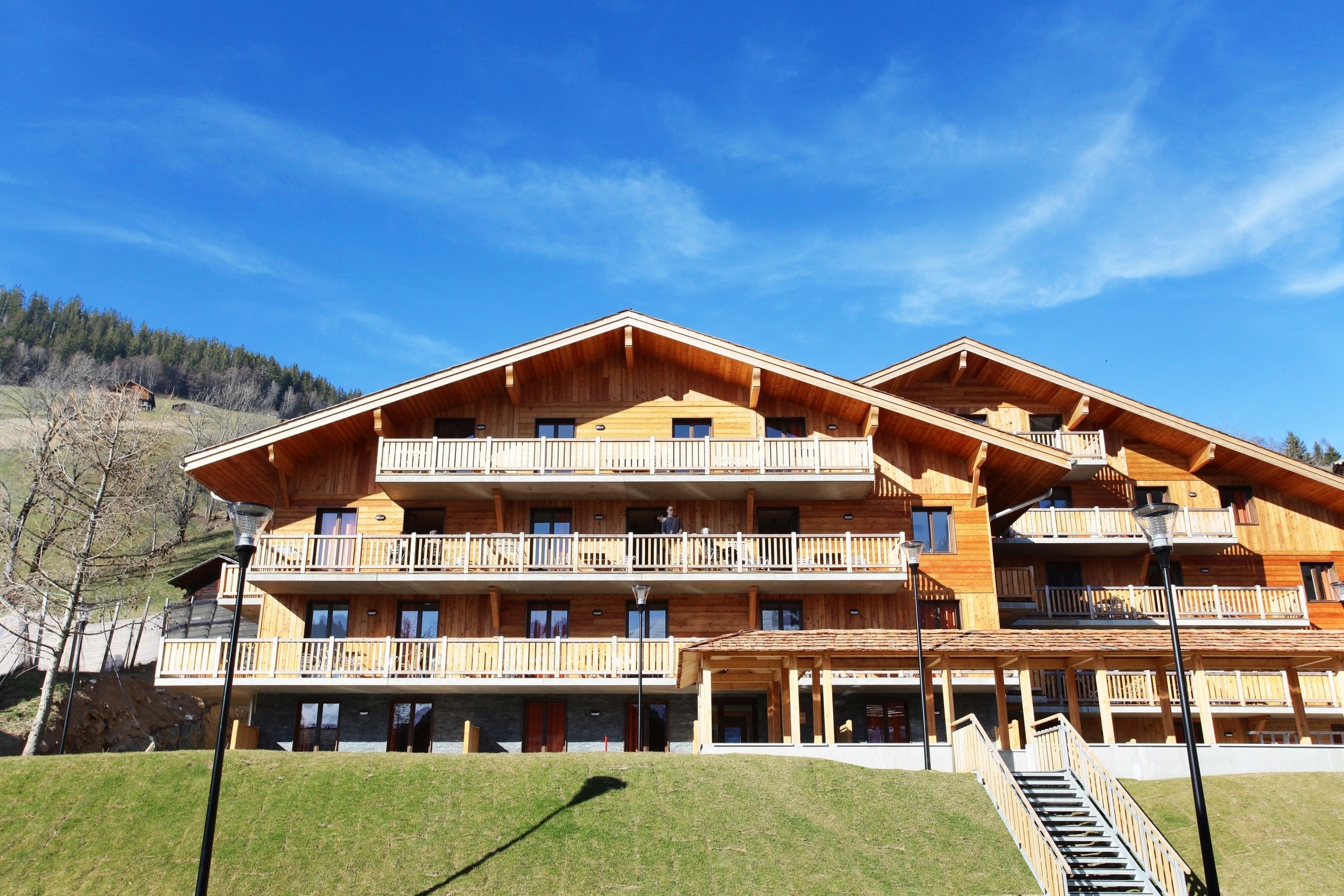 A multi-story wooden building with balconies, a covered entrance, and a staircase leading to the upper floors.