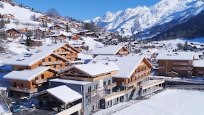 A snow-covered mountain village with wooden buildings, a ski slope, and a clear blue sky.