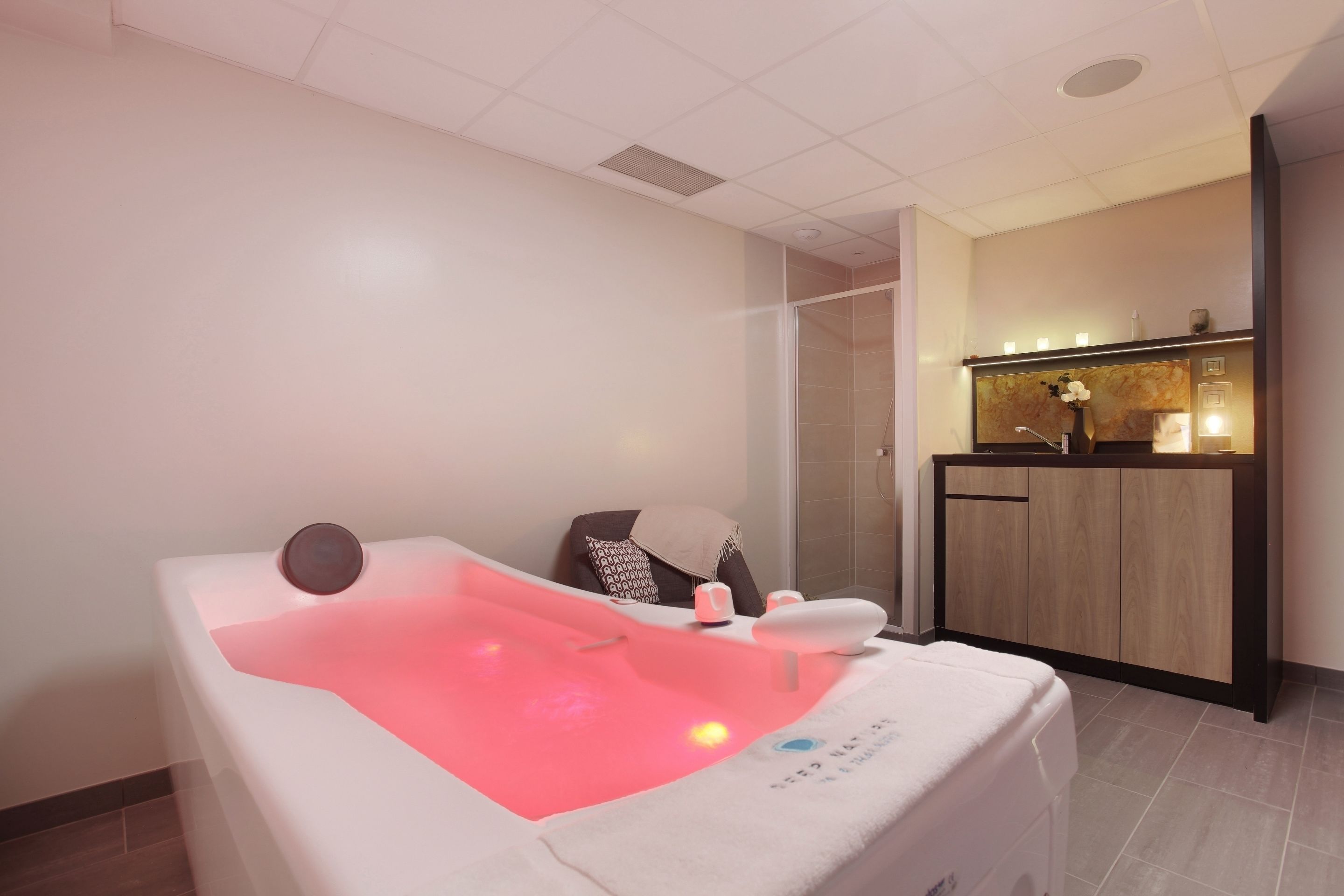 Ein Spa-Raum mit Massagetisch, separatem Duschbereich und einem Holzbadezimmer-Waschtisch mit Spiegel.