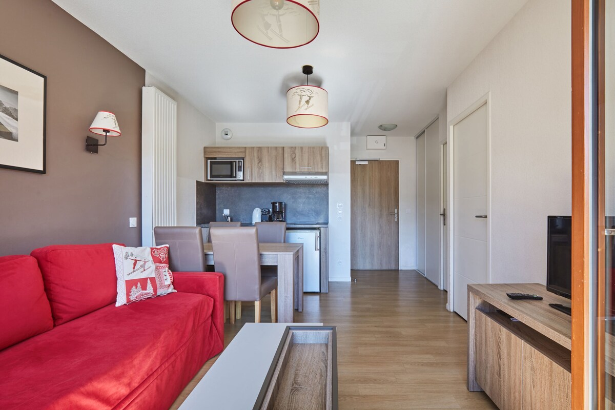 A compact living space with a red sofa, a dining area, a kitchenette, and a television.