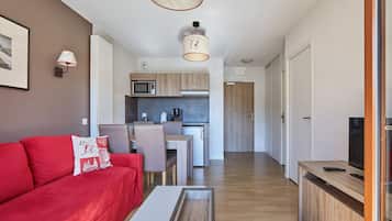 Un espace de vie compact comprenant un canapé rouge, un coin repas, une kitchenette et un téléviseur.