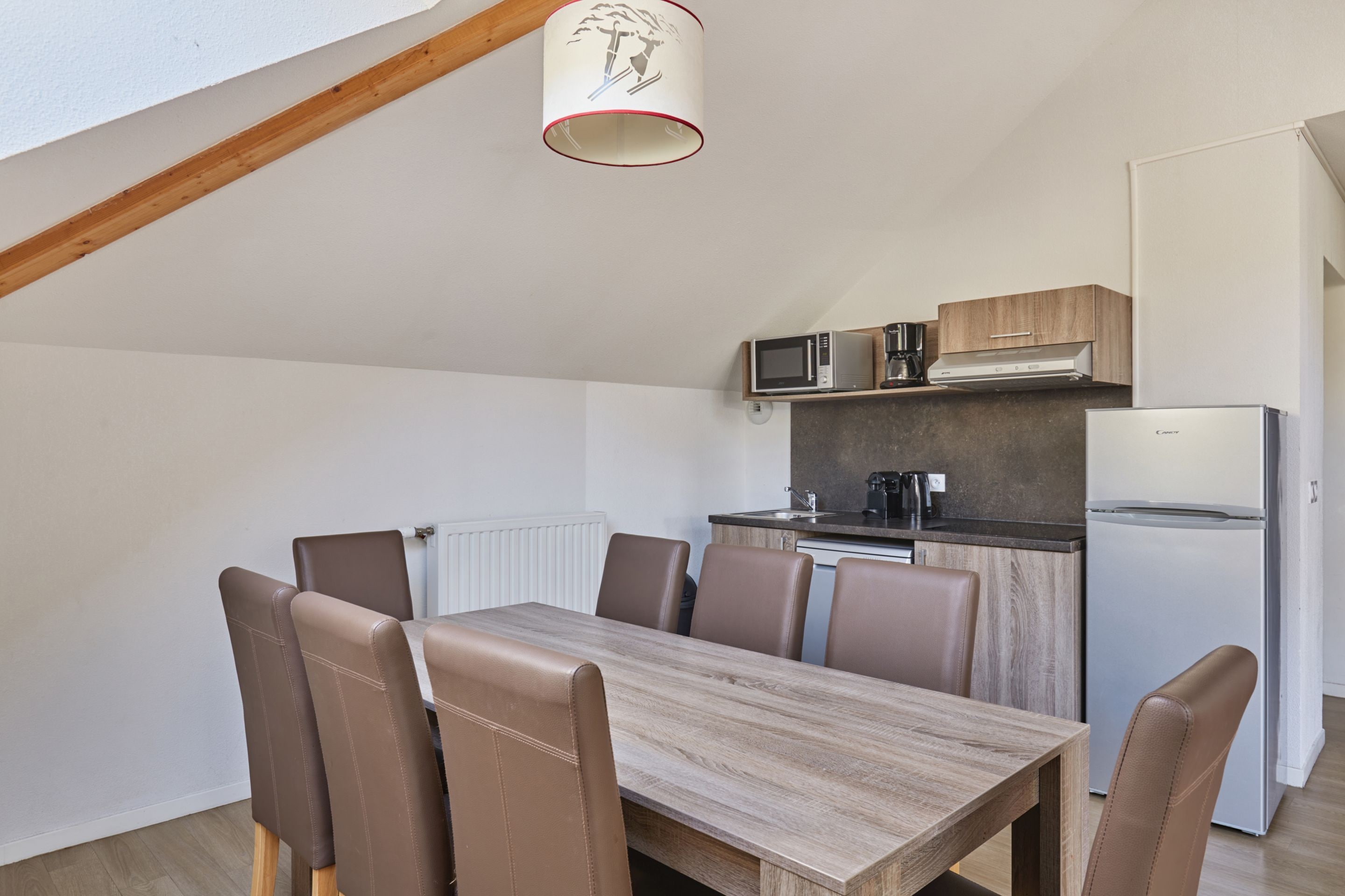 A compact kitchen with modern appliances, a dining table with chairs, and a sloped ceiling with a light fixture.