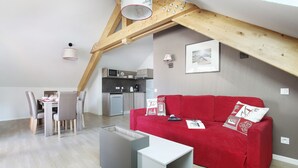 A modern loft apartment with a dining area, kitchen, and a red sofa with patterned cushions.