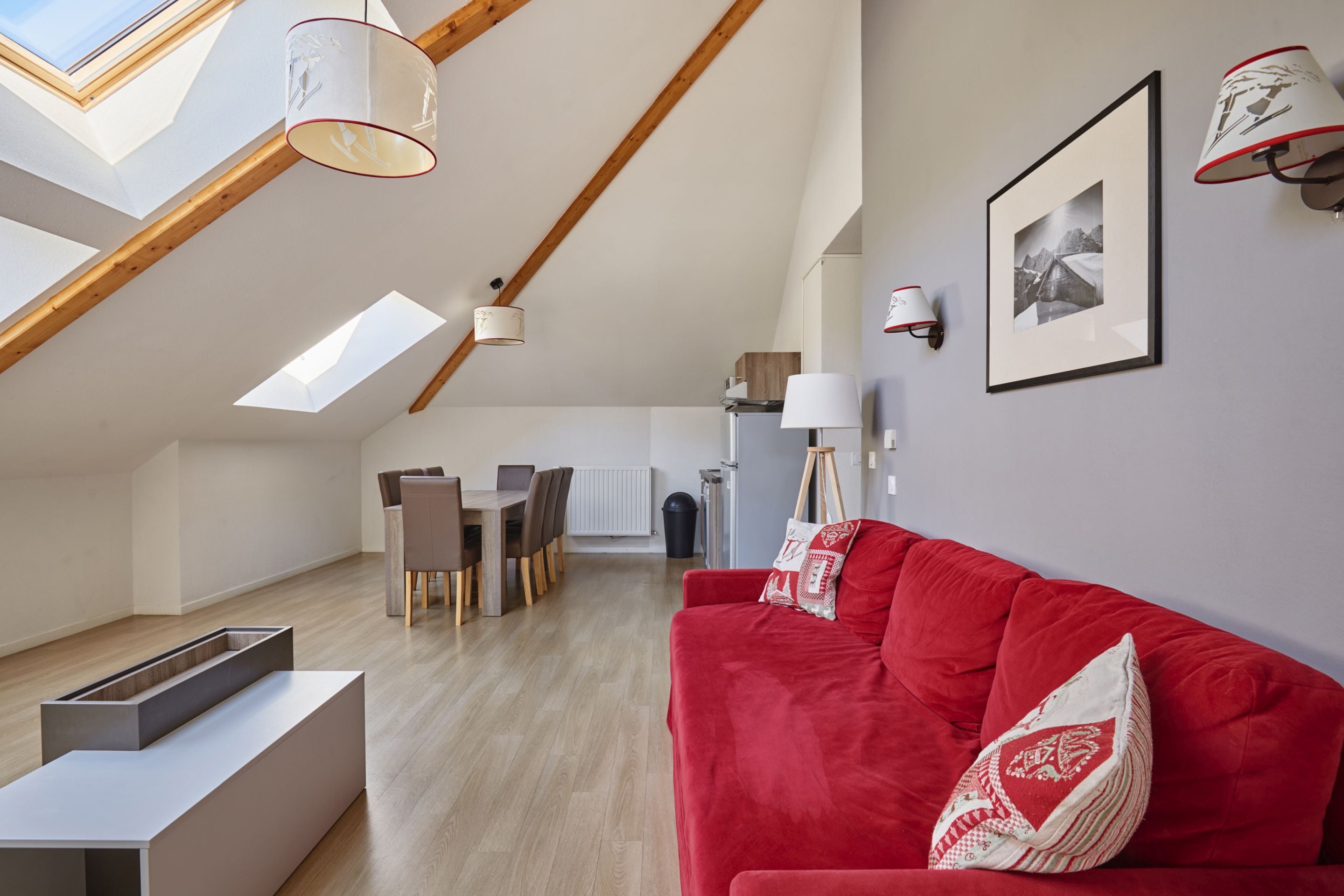 A modern loft with a red sofa, wooden dining table, and a view of the sky through skylights.