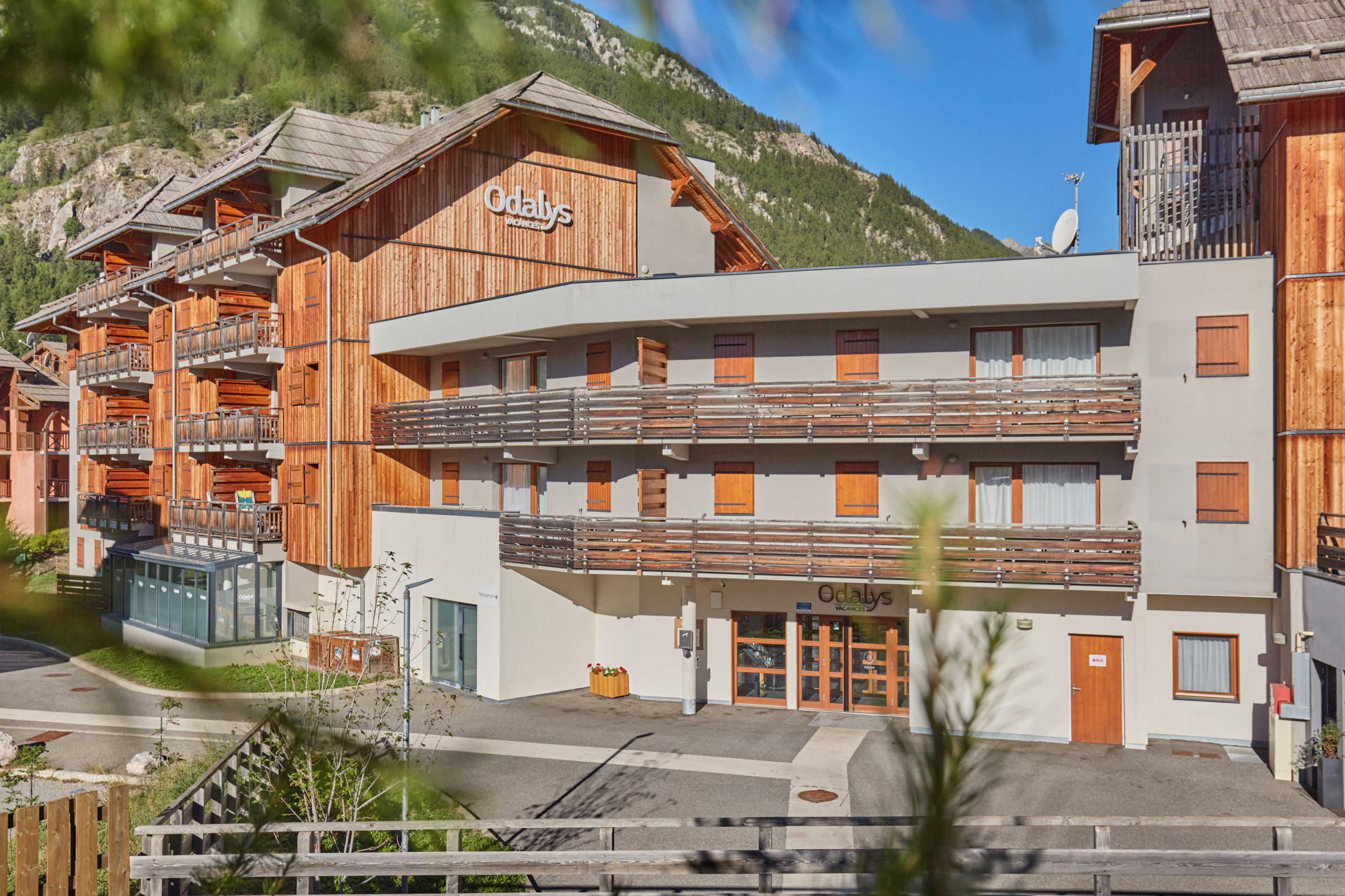 A hotel with a wooden facade, balconies, and a sign indicating 'Vacances.'