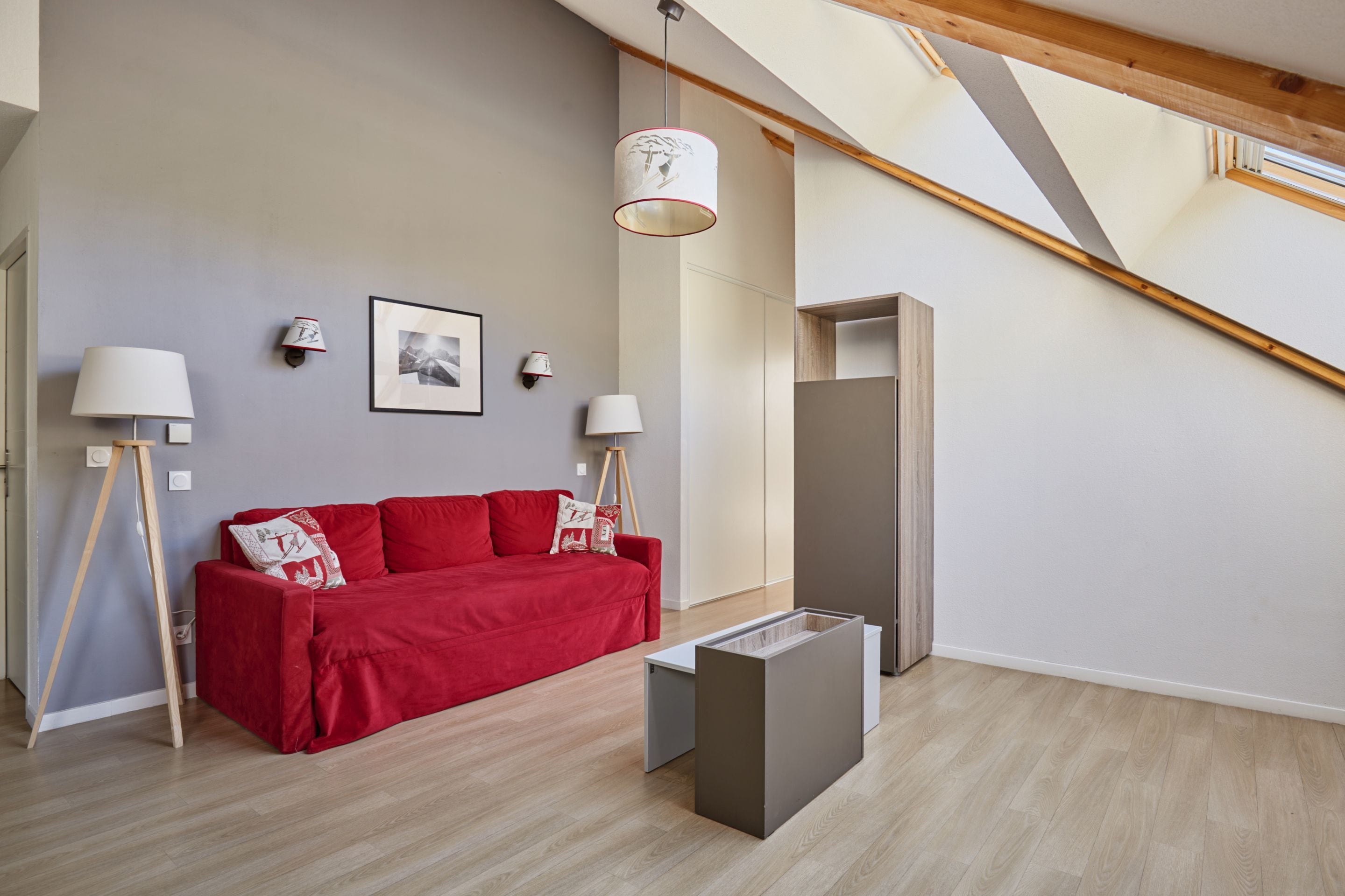 A modern living room with a red sofa, two wall-mounted lamps, a framed photograph, and a wooden floor.