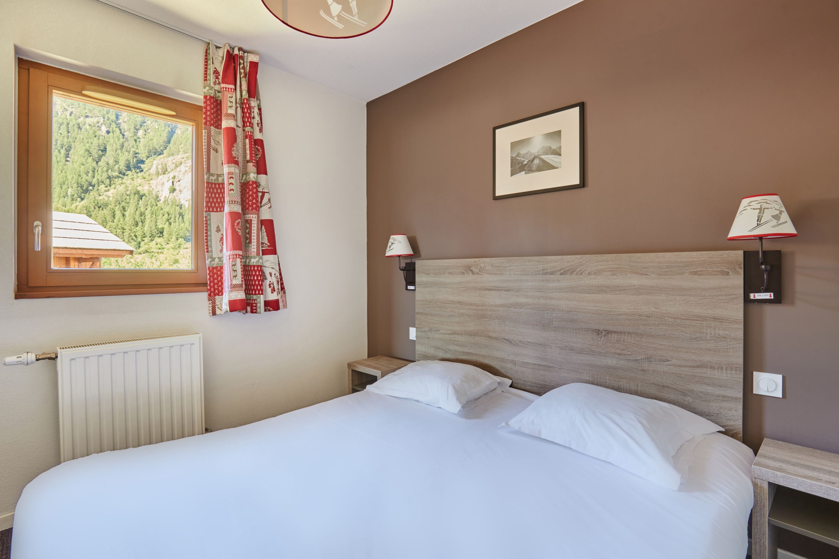Een slaapkamer met een bed, een raam met gordijnen, een wandlamp en een ingelijst schilderij.