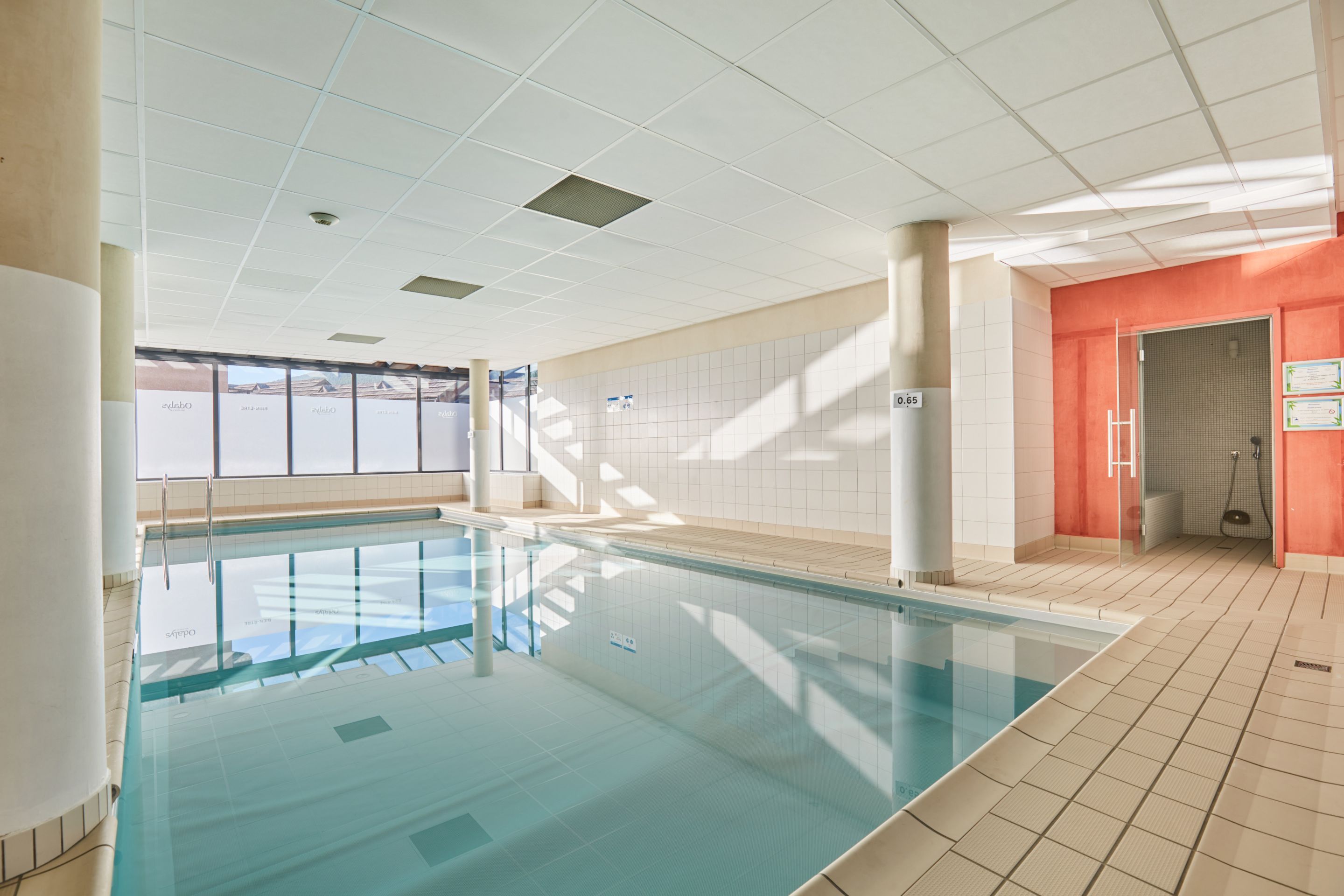 Una piscina con agua cristalina, rodeada de paredes con azulejos e iluminación empotrada en el techo.