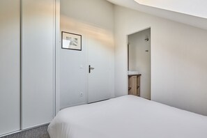 A hotel room with a bed, a door with a picture frame, a bathroom with a sink, and a mirror. - Résidence Odalys Aquisana (La Salle-les-Alpes)