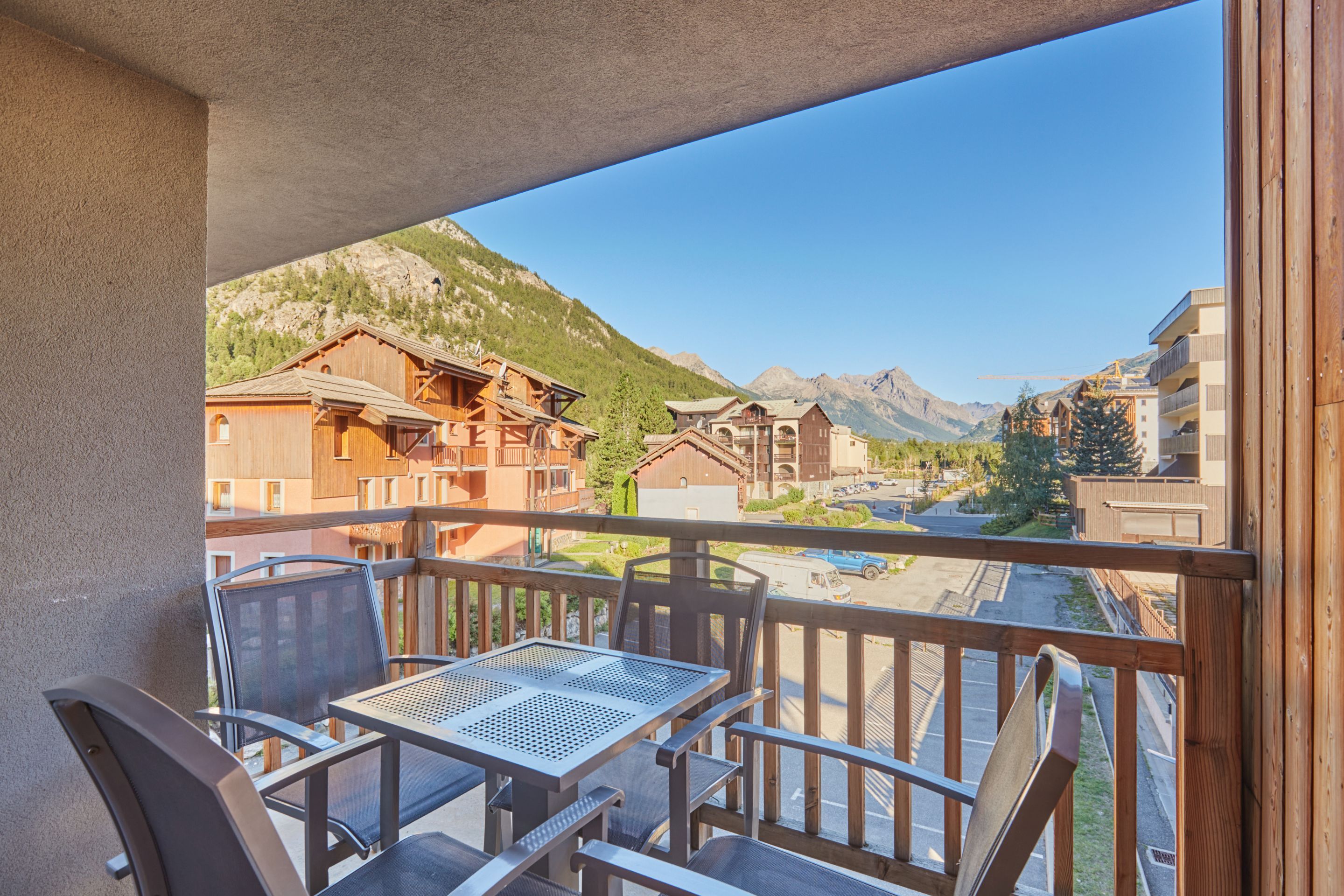 Un balcon avec une table et des chaises, donnant sur un paysage montagneux parsemé de bâtiments.