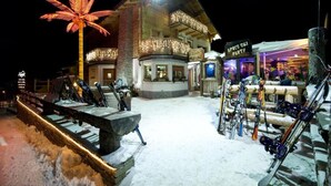 A snow-covered outdoor area with a ski lift, a building with a sign reading "APRES SUI PARTY", and a palm tree illuminated by lights. - Hotel Alegra (Livigno)