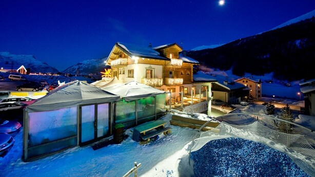 A snow-covered mountain resort with a large lodge featuring balconies and a well-lit entrance. - Hotel Alegra (Livigno)