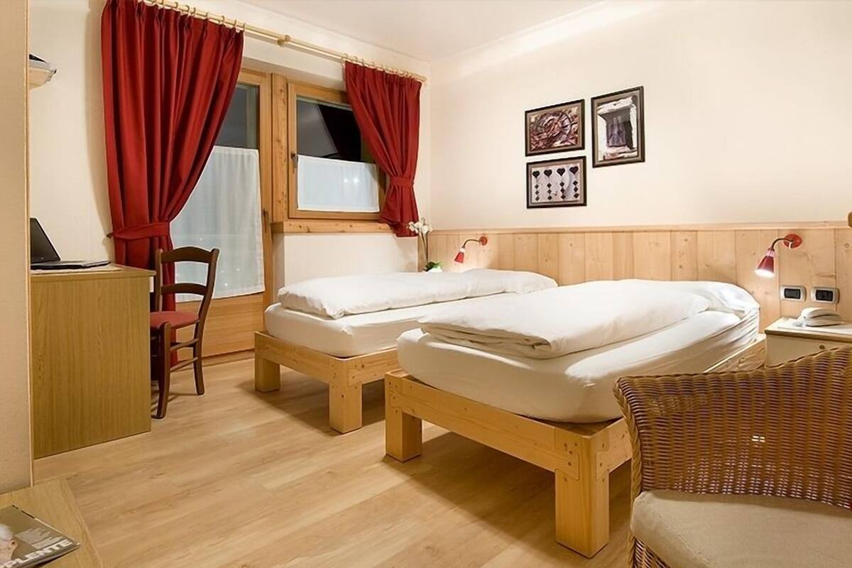 A room with two wooden beds, a desk with a laptop, a chair, and a wicker chair.