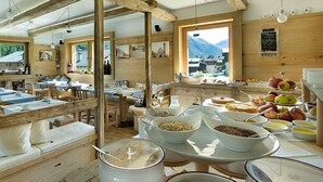 A rustic dining area with wooden tables and benches, a buffet with various food items, and a view of mountains through large windows. - Hotel Alegra (Livigno)