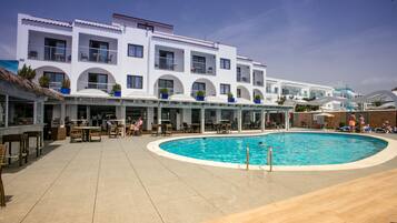 A modern hotel with a swimming pool, outdoor seating, and a covered patio area.