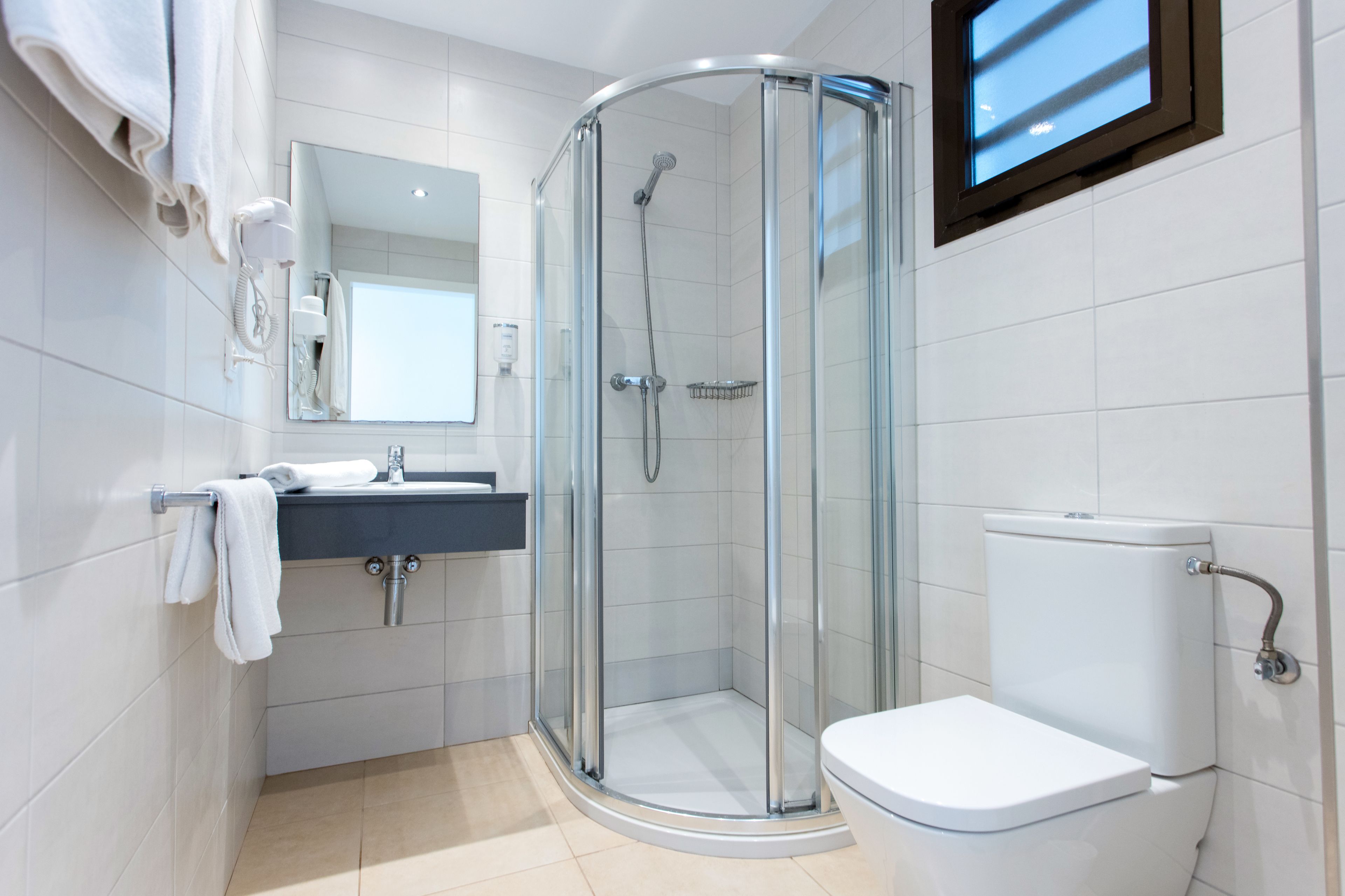 A modern bathroom with a glass-enclosed shower, a white toilet, and a sink with a mirror above it.