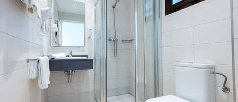 Un baño moderno con ducha de vidrio, inodoro blanco y lavabo con espejo.
