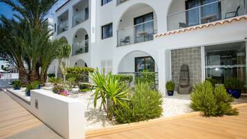 A modern building with multiple balconies, white walls, and a landscaped garden with various plants.