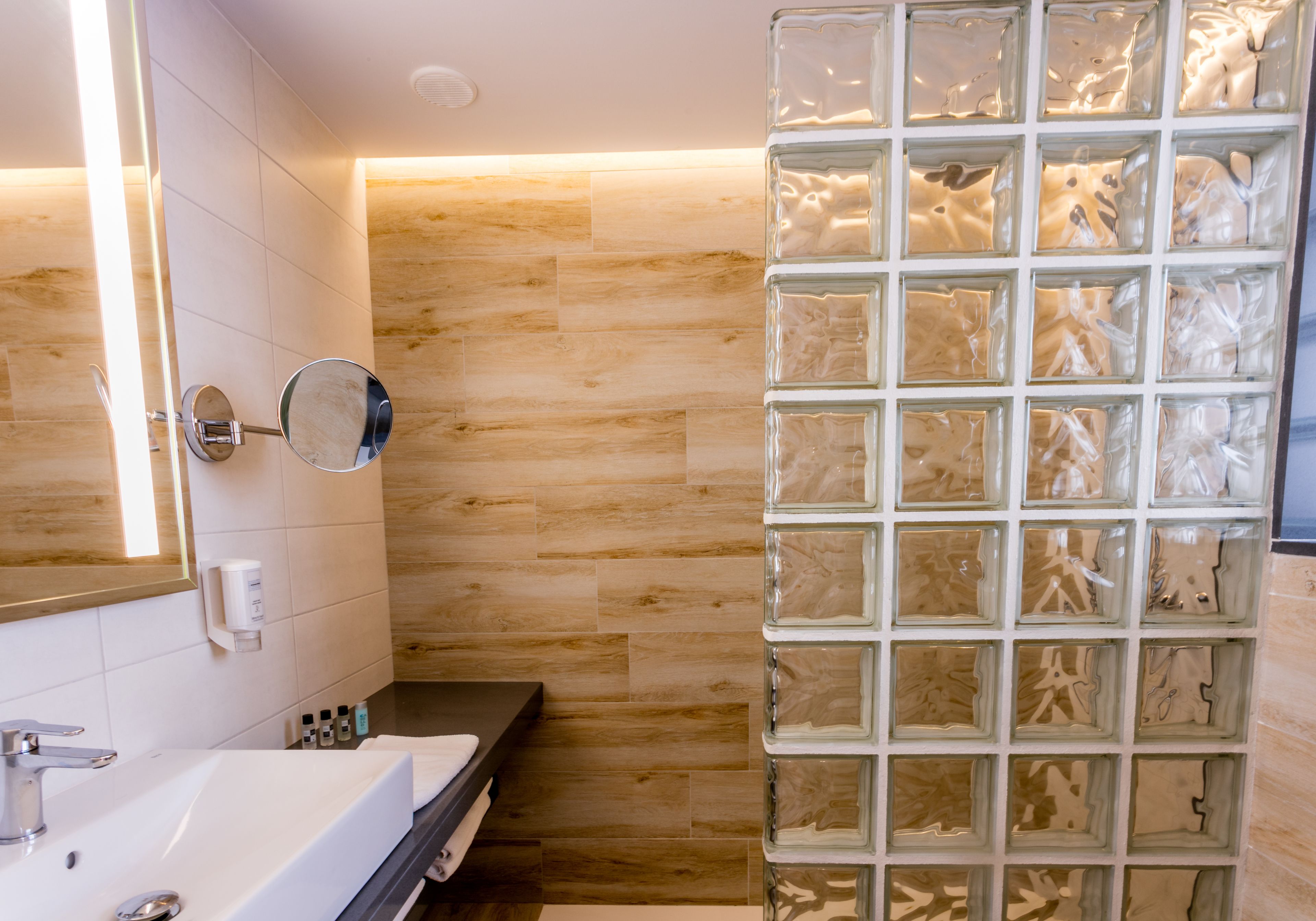 A modern bathroom with a large mirror, a white sink, and a glass shower enclosure.