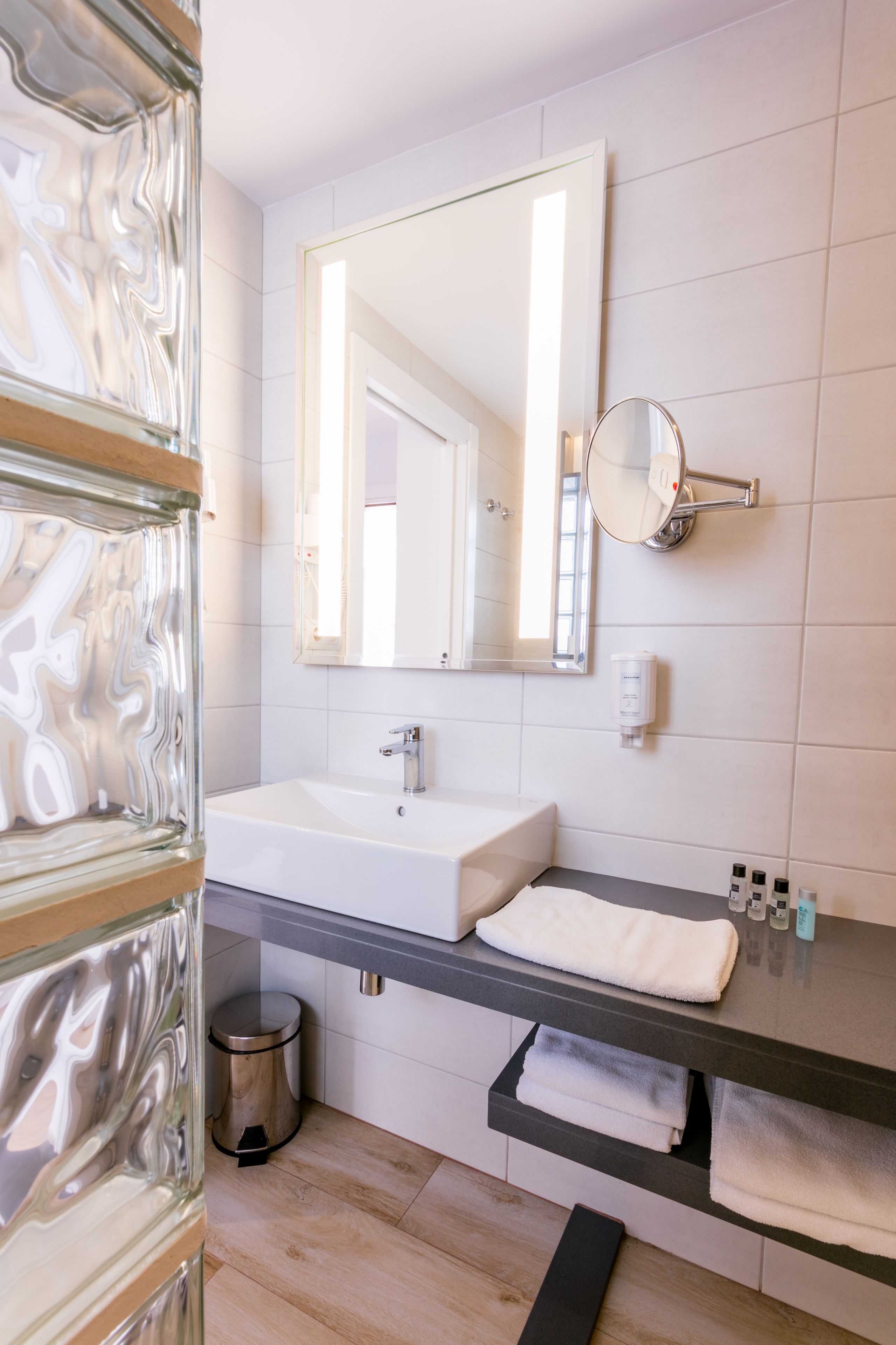 Un baño moderno con un espejo grande, baldosas blancas, un lavamanos y un perchero para toallas.