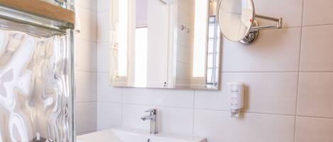 Un baño moderno con un espejo grande, baldosas blancas, un lavamanos y un perchero para toallas.