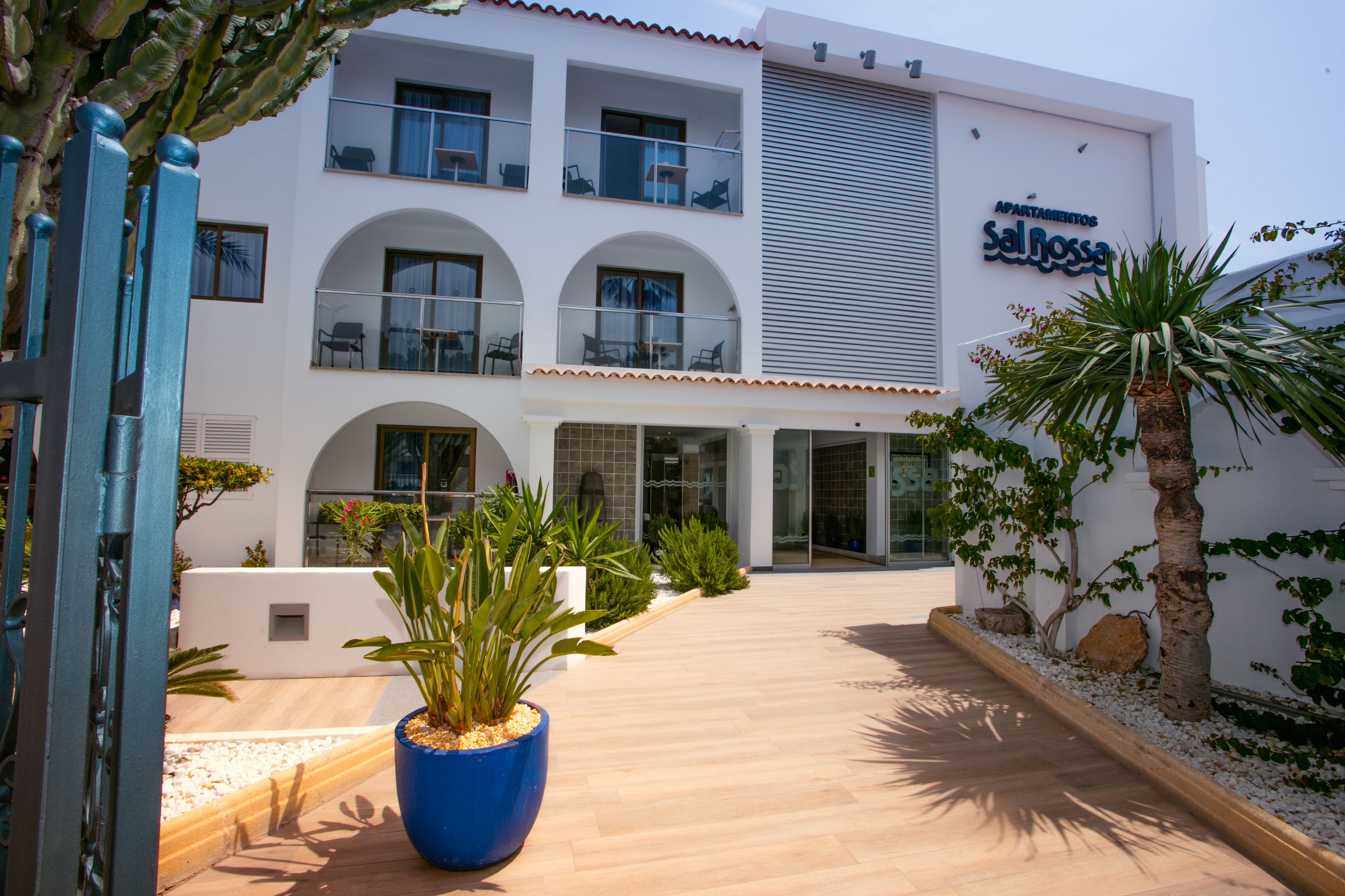 A modern building with a sign reading "Apartamentos Sal Bossa". It features a central courtyard with potted plants and a wooden walkway.