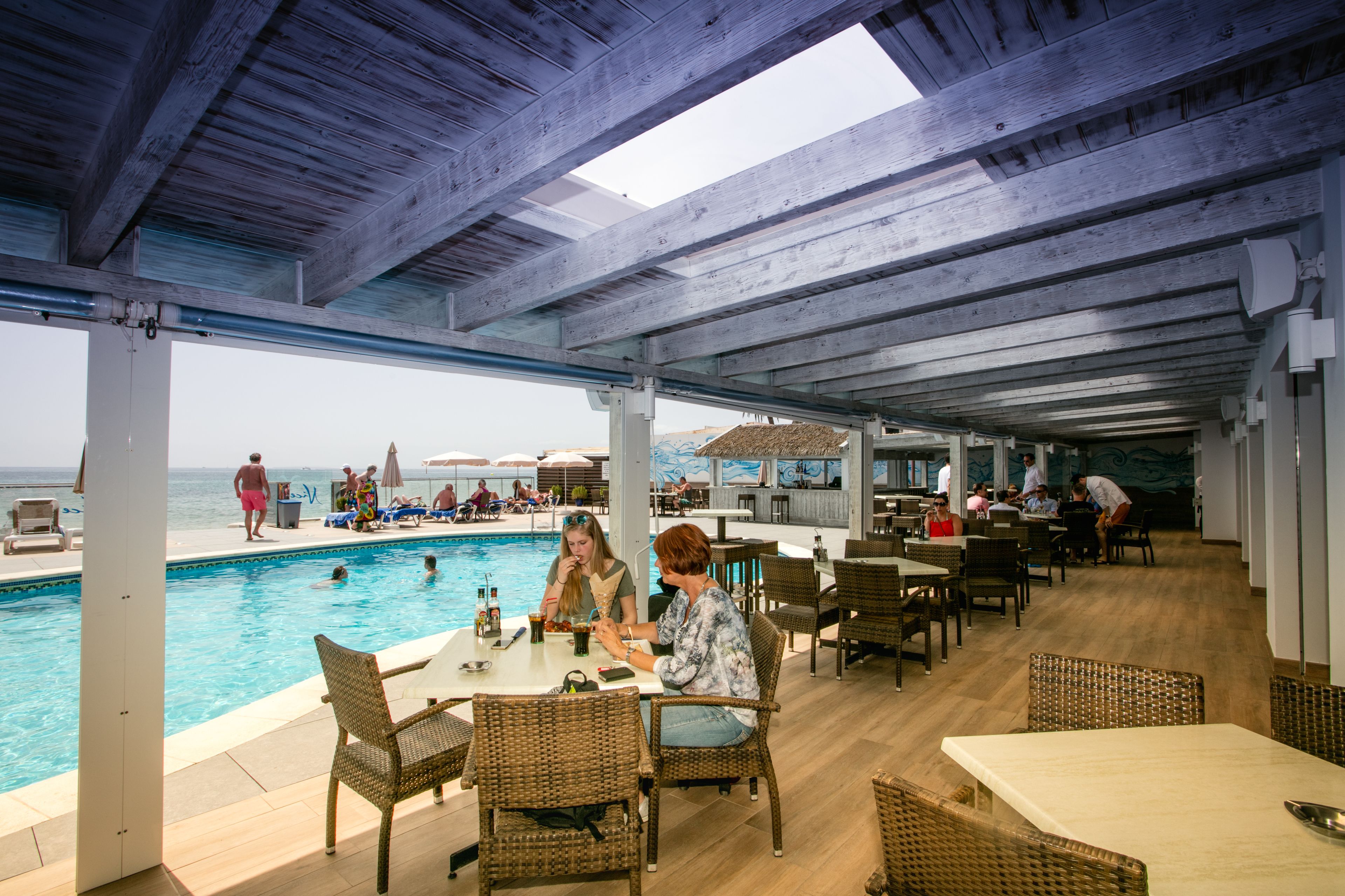 Zona junto a la piscina con mesas y sillas, con vistas a una piscina y una playa.