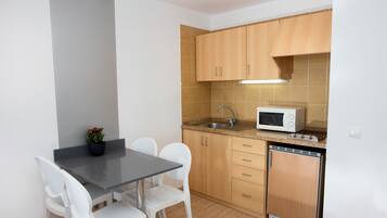A compact kitchen with a microwave, sink, and wooden cabinets. There is a small dining table with chairs and a potted plant.
