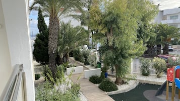 A balcony with a view of a landscaped garden, including palm trees, a playground, and a pathway.