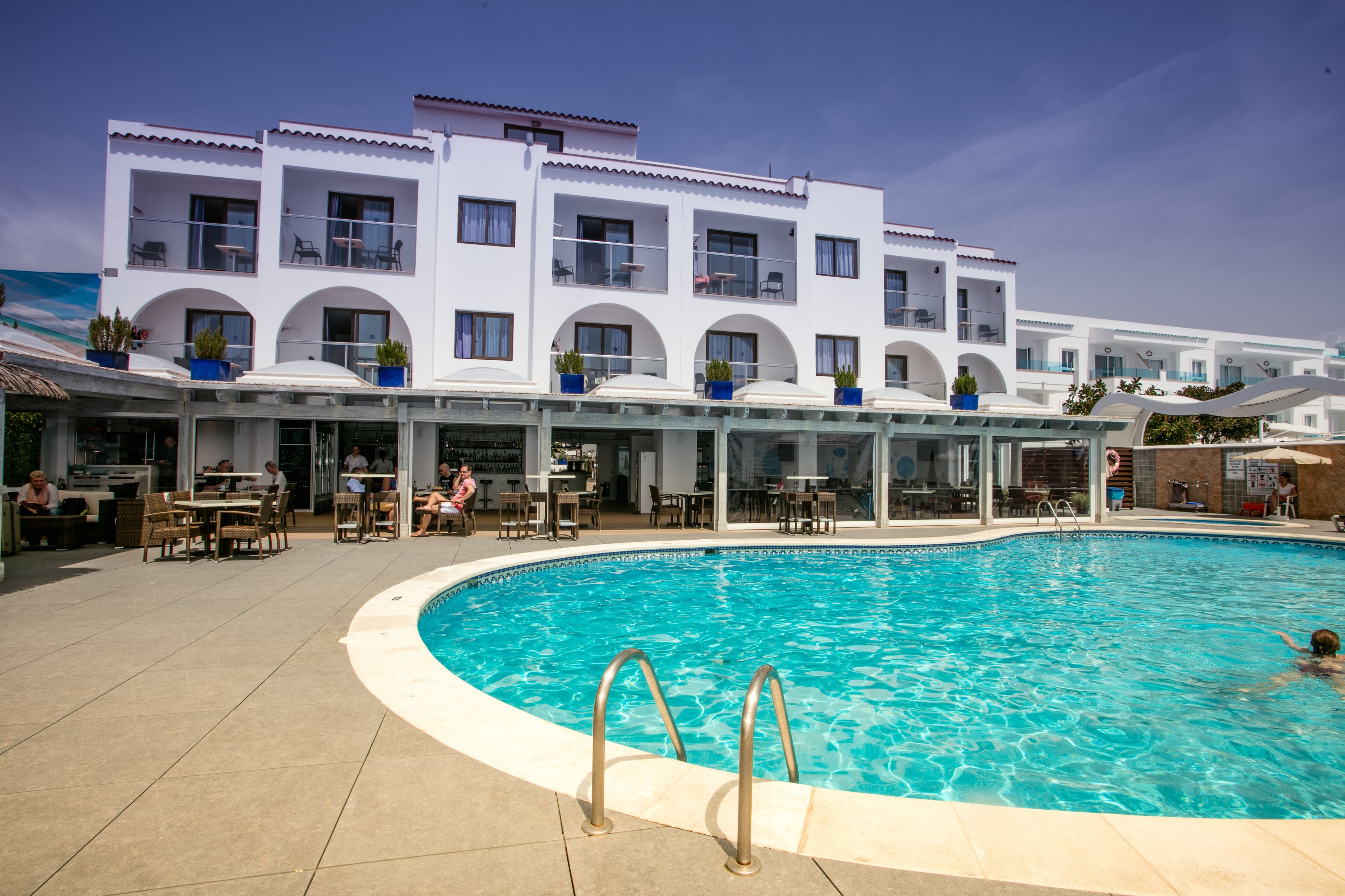 Un hotel con piscina, mobiliario exterior y varios balcones.