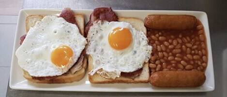 Un plato de desayuno con dos huevos fritos, tocino, tostadas, frijoles horneados y una salchicha.