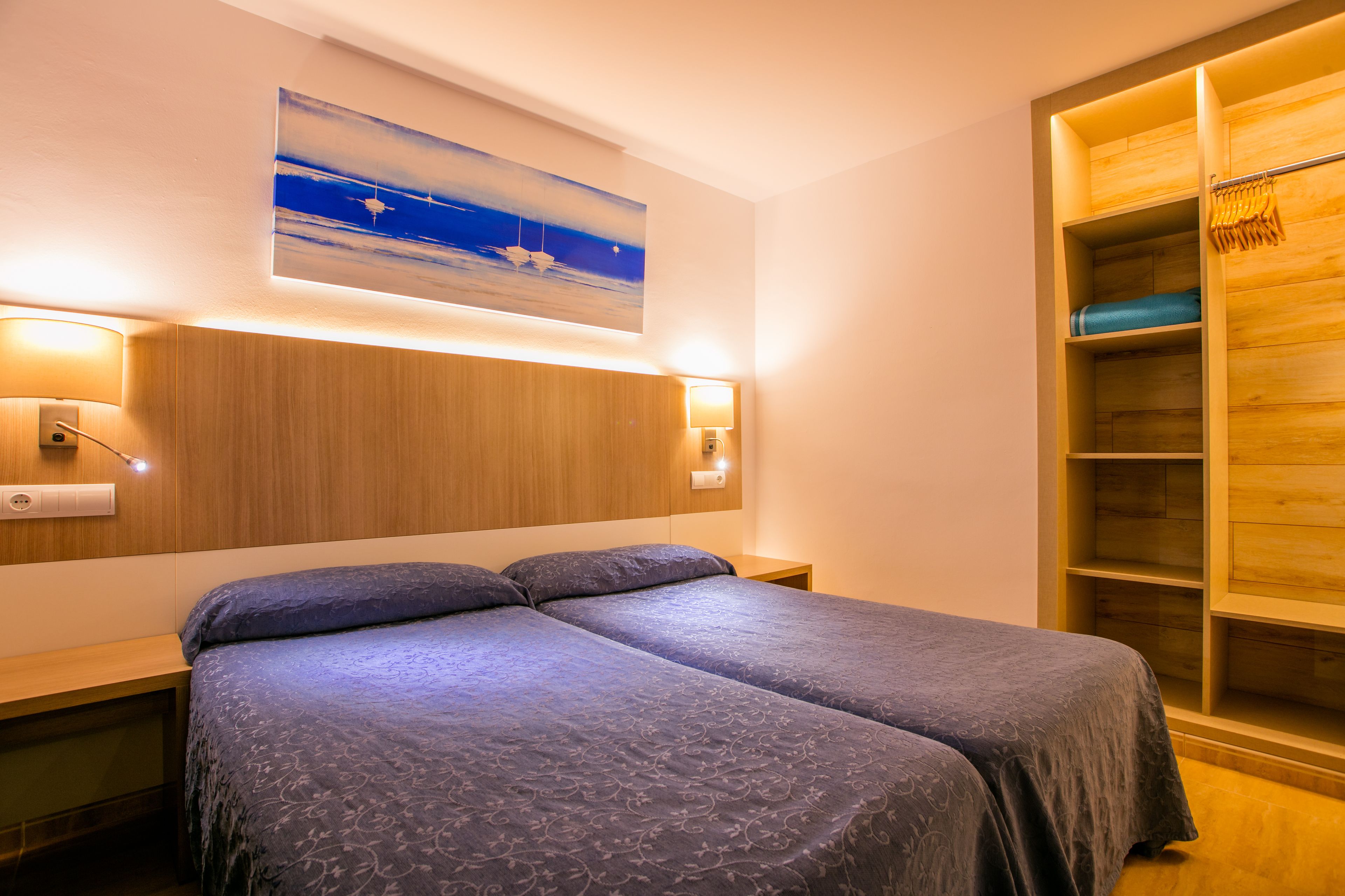 Ein Doppelbett mit Kopfteil, Nachttische, ein an der Wand hängendes Bild und ein Holzschrank mit Spiegel.